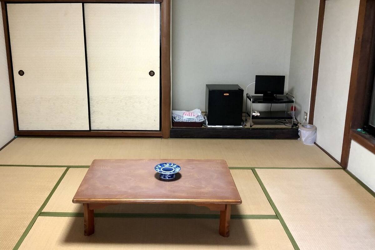 A tatami mat room with a wooden table, a black TV stand, and a sliding door.