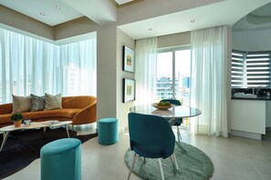 Ein modernes Wohnzimmer mit einer Couch, einem Couchtisch und einem Esstisch mit Stühlen. Es gibt eine Küchenzeile mit Spüle und Schränken.