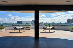 Eine Dachterrasse mit Blick auf die Stadt, zwei Tische mit Stühlen und Blumentöpfen.