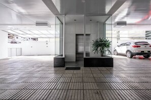 A modern building entrance with a glass facade, a potted plant, and a car parked outside. - ®{ArtDeco~Exclusive} @DowntownSD +Gym+Piantini (Santo Domingo)