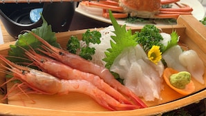 A wooden tray with seafood, including shrimp, sashimi, and a green garnish.