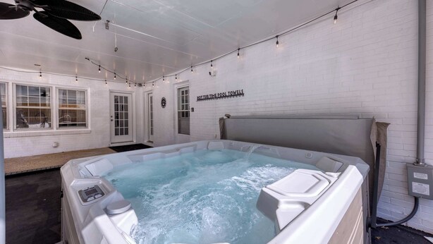 Ein Whirlpool mit einem Schild, auf dem ‘HOT TUB TIME POOL TOWELS’ steht, in einem Raum mit weißen Ziegelwänden, einem Deckenventilator und Lichterketten.
