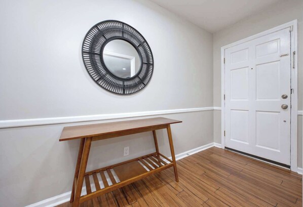 A hallway with a wooden floor, a white door, and a wall-mounted mirror.