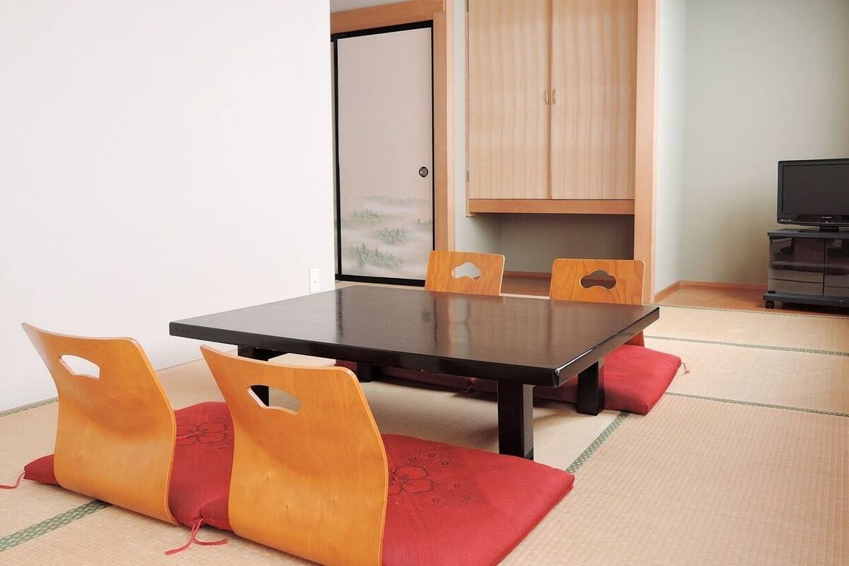 Um quarto com piso de tatame, uma mesa baixa e cadeiras em estilo tradicional japonês.