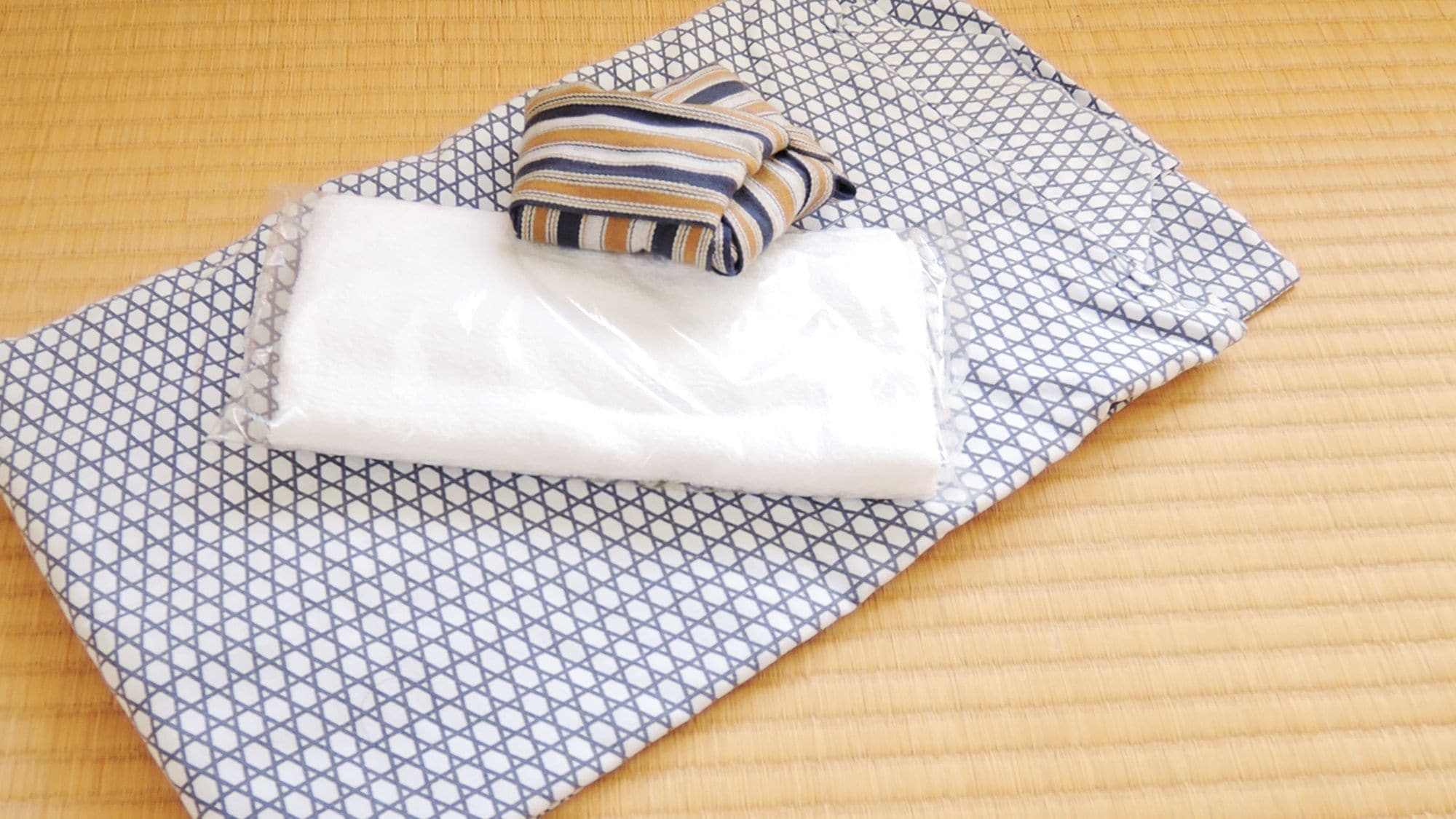 Une serviette blanche soigneusement pliée et un coussin à rayures reposent sur un couvre-lit à motifs.