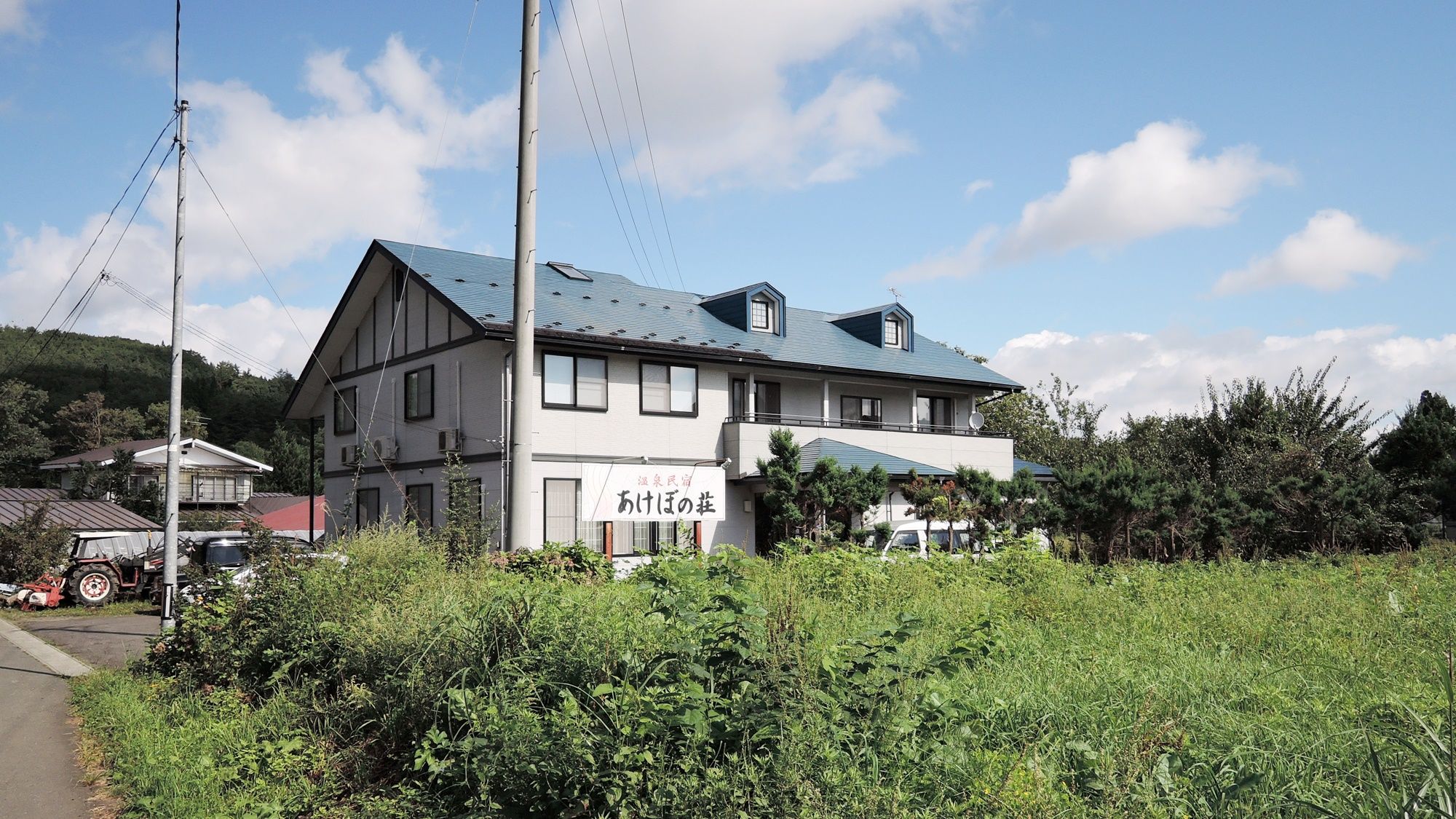 A two-story building with a sign in front, surrounded by greenery and a clear sky.
