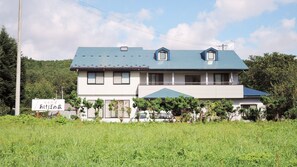 A two-story building with a blue roof, surrounded by greenery and a signboard. - Oshuku Onsen Minshuku Akebonoso (Shizukuishi)