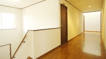 Un pasillo con suelo de madera, paredes blancas y una puerta.