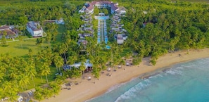 Luftaufnahme eines Resorts mit einem zentralen Pool, umgeben von Palmen und direkt am Strand.