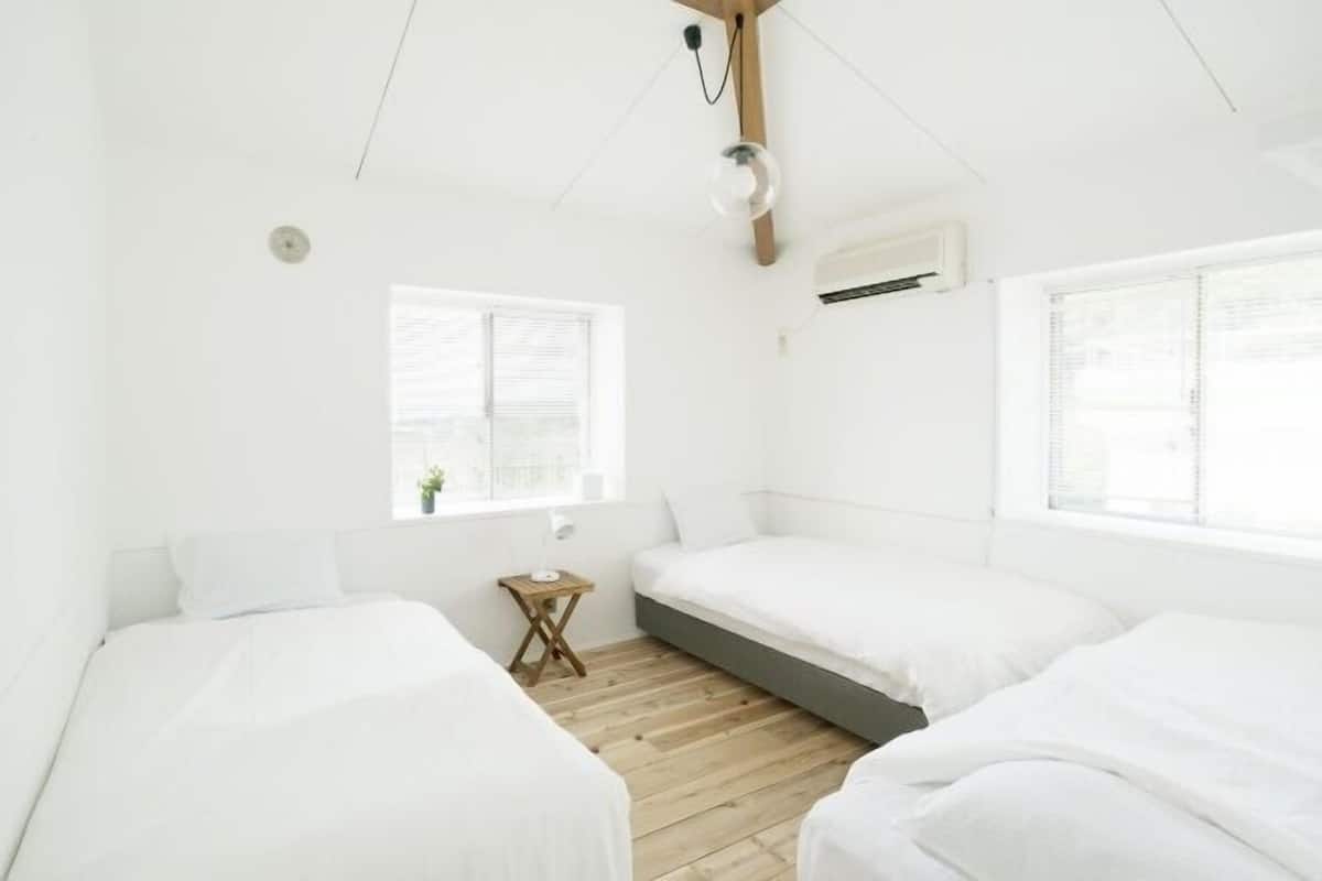 Habitación minimalista con tres camas, una mesita y una ventana.