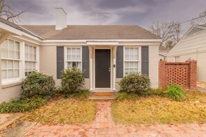 A single-story house with a front door, two windows with shutters, a brick pathway leading to the door, and a small front yard with shrubs. - Near Downtown - The Delightful Double - Units A&B (Columbus)