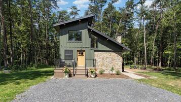 Une cabane à deux étages avec un mur en pierre, une terrasse en bois et une allée gravillonnée.