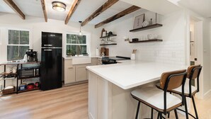 Een keuken met een groot eiland, houten balken, witte kastjes en een inbouwoven.