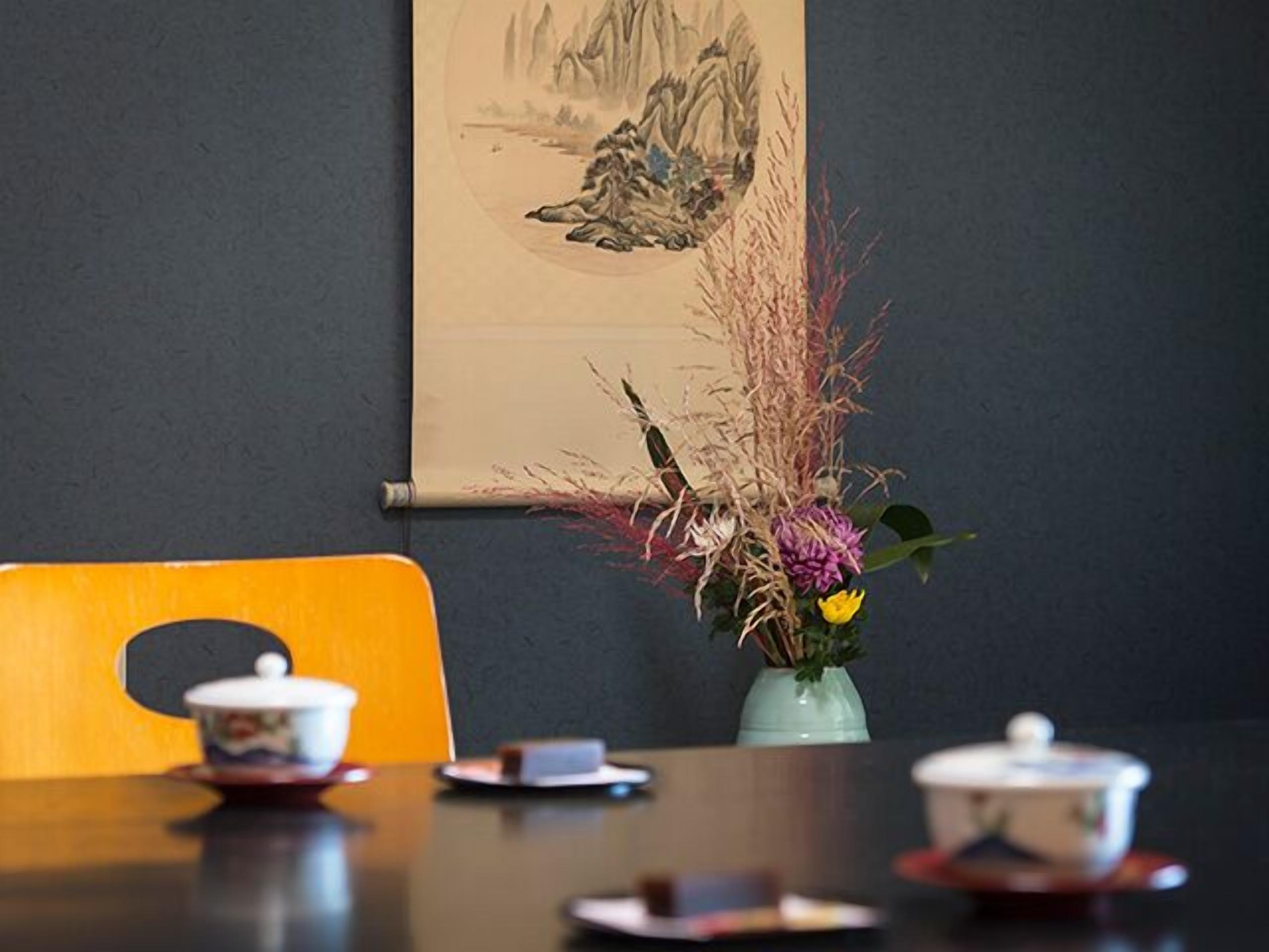 A dining table with a vase of dried plants, a teapot, and a cup on a coaster.