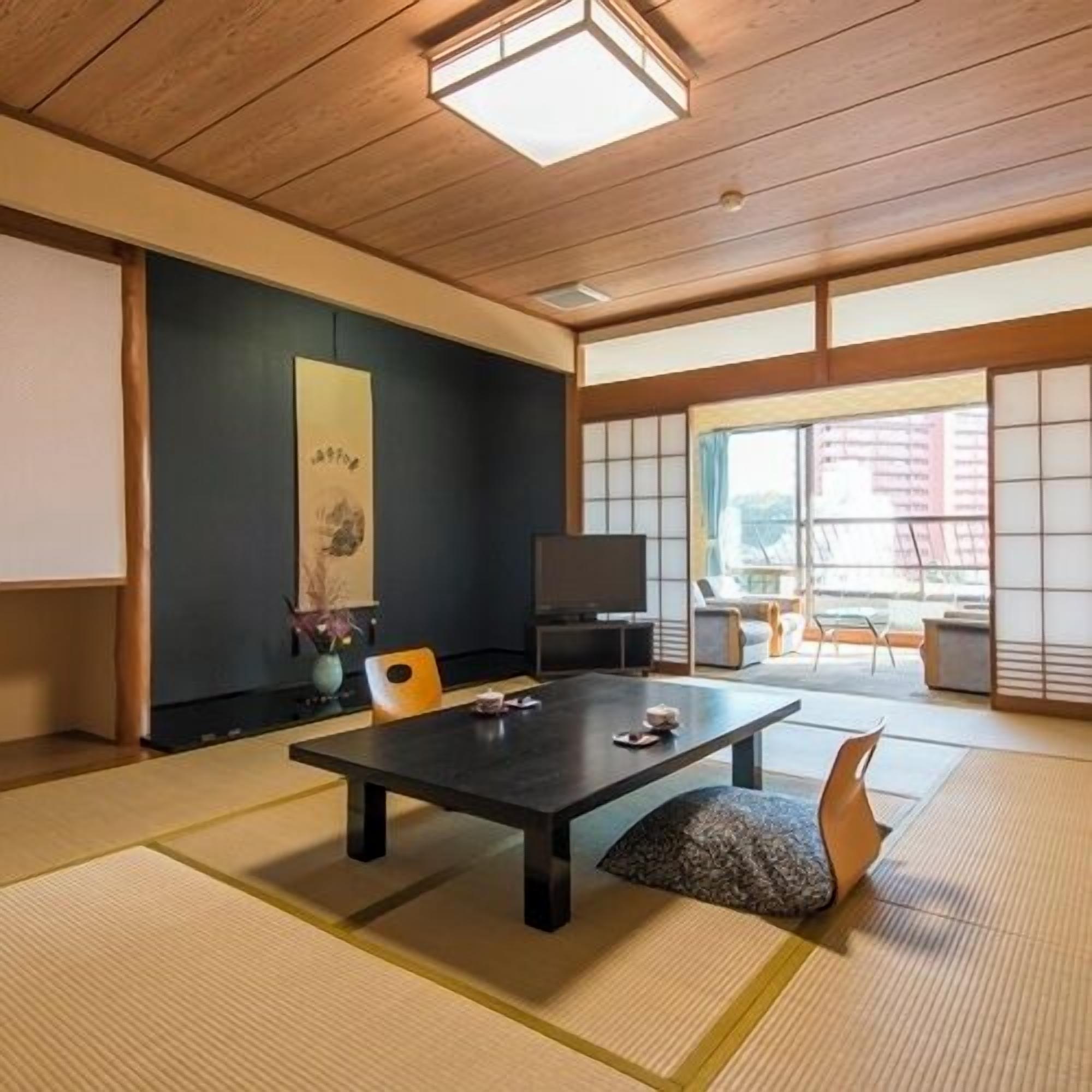 Ein traditioneller japanischer Raum mit Tatami-Böden, einem niedrigen Tisch, einem Fernseher und Schiebetüren.