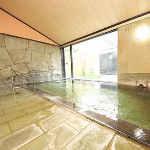 Ein Innenpool mit Steinwänden, einer klaren Glasscheibe und Blick auf Grünfläche.