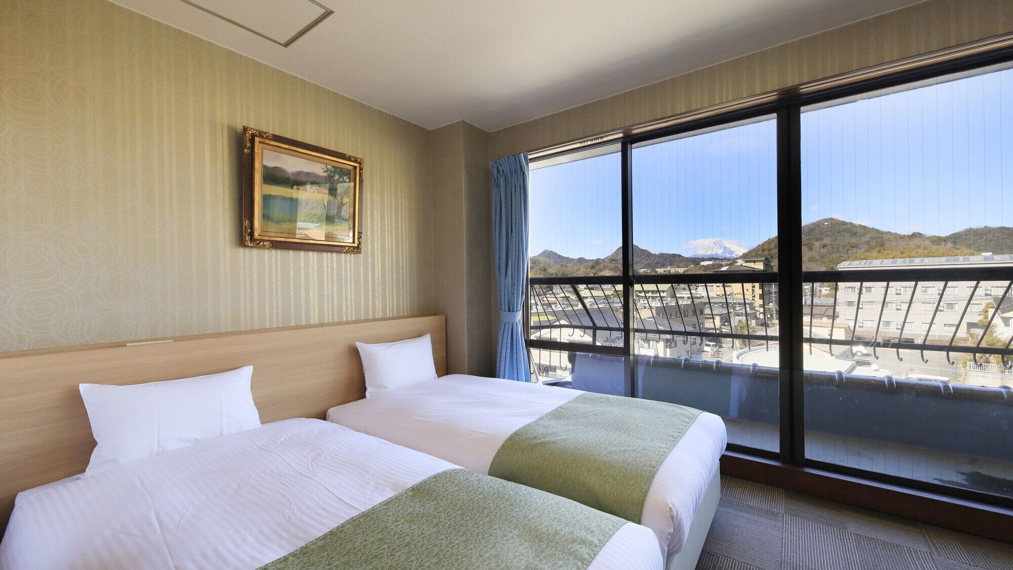 A hotel room with a large window, a bed, and a painting on the wall.