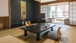 Una habitación japonesa tradicional con suelo de tatami, una mesa de madera oscura, un televisor y una puerta corrediza que da a un balcón.