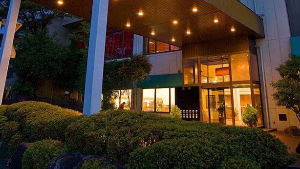 Entrada de hotel con zona cubierta, varios pisos y fachada bien iluminada.