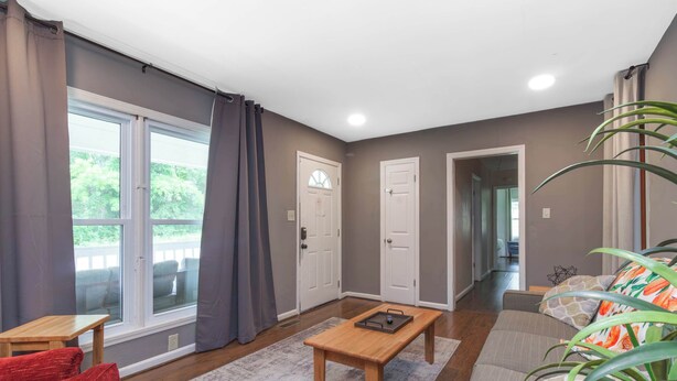 Ein Wohnzimmer mit Couchtisch aus Holz, einem roten Sofa, einem grauen Sofa und einem großen Fenster mit Vorhängen.