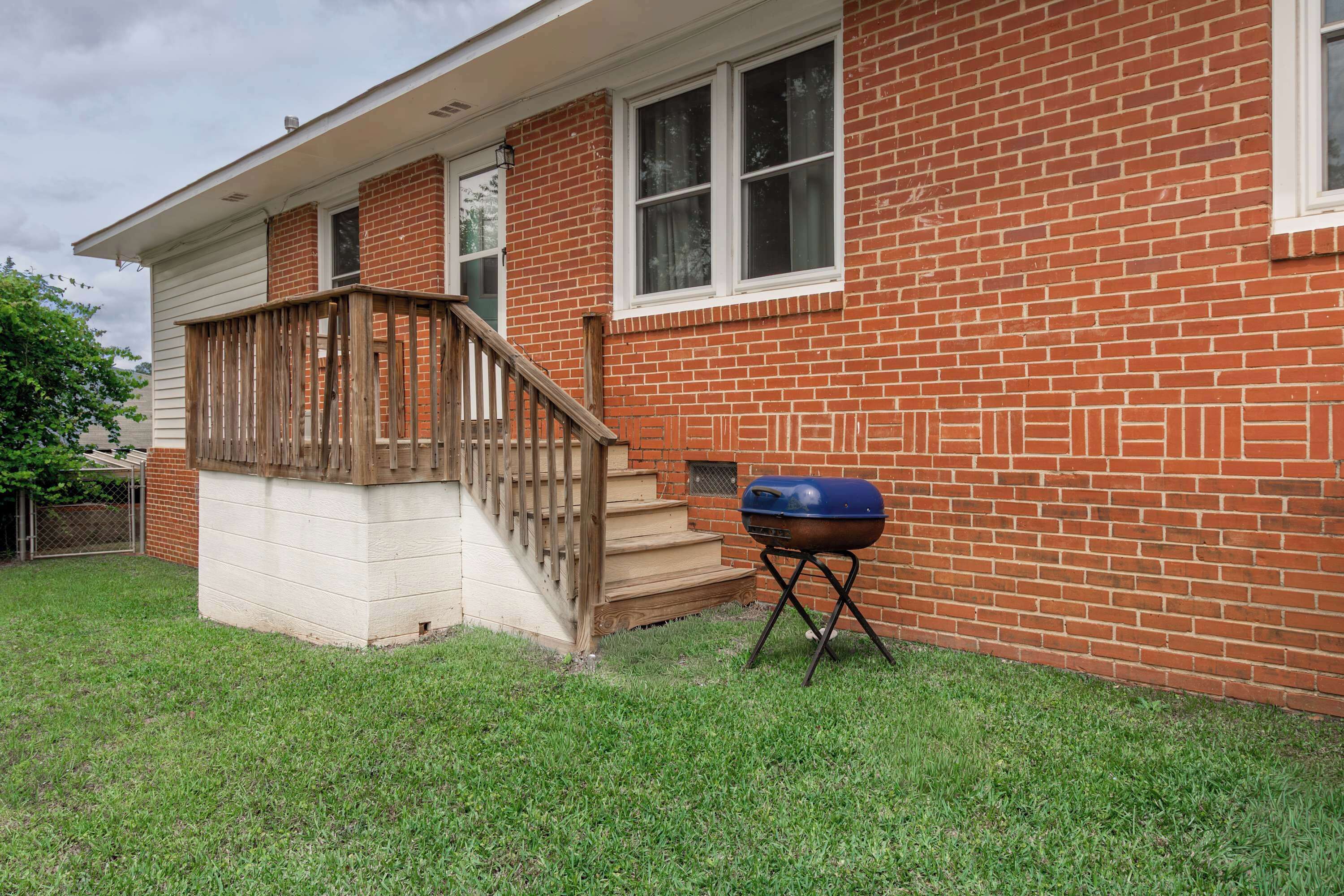 A brick house with a wooden front porch and a barbecue grill in the yard.