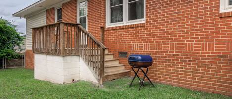 A brick house with a wooden front porch and a barbecue grill in the yard.