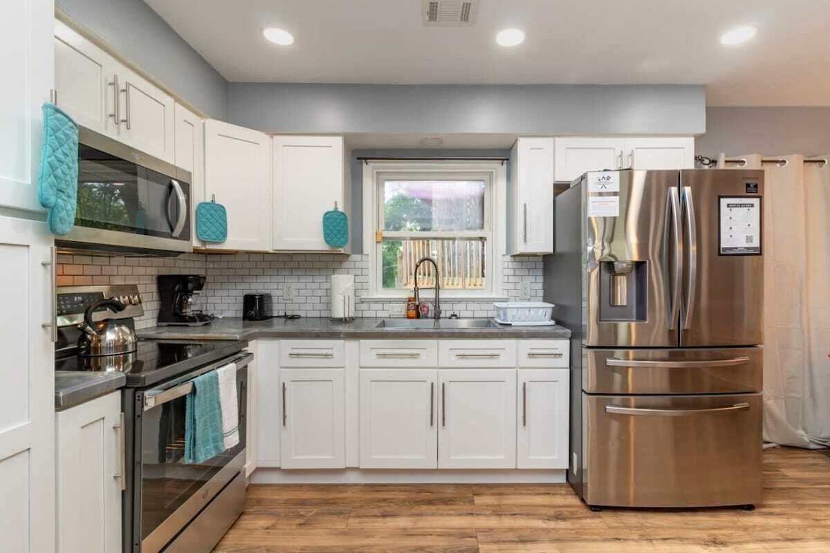 A modern kitchen with white cabinets, stainless steel appliances, and a window.