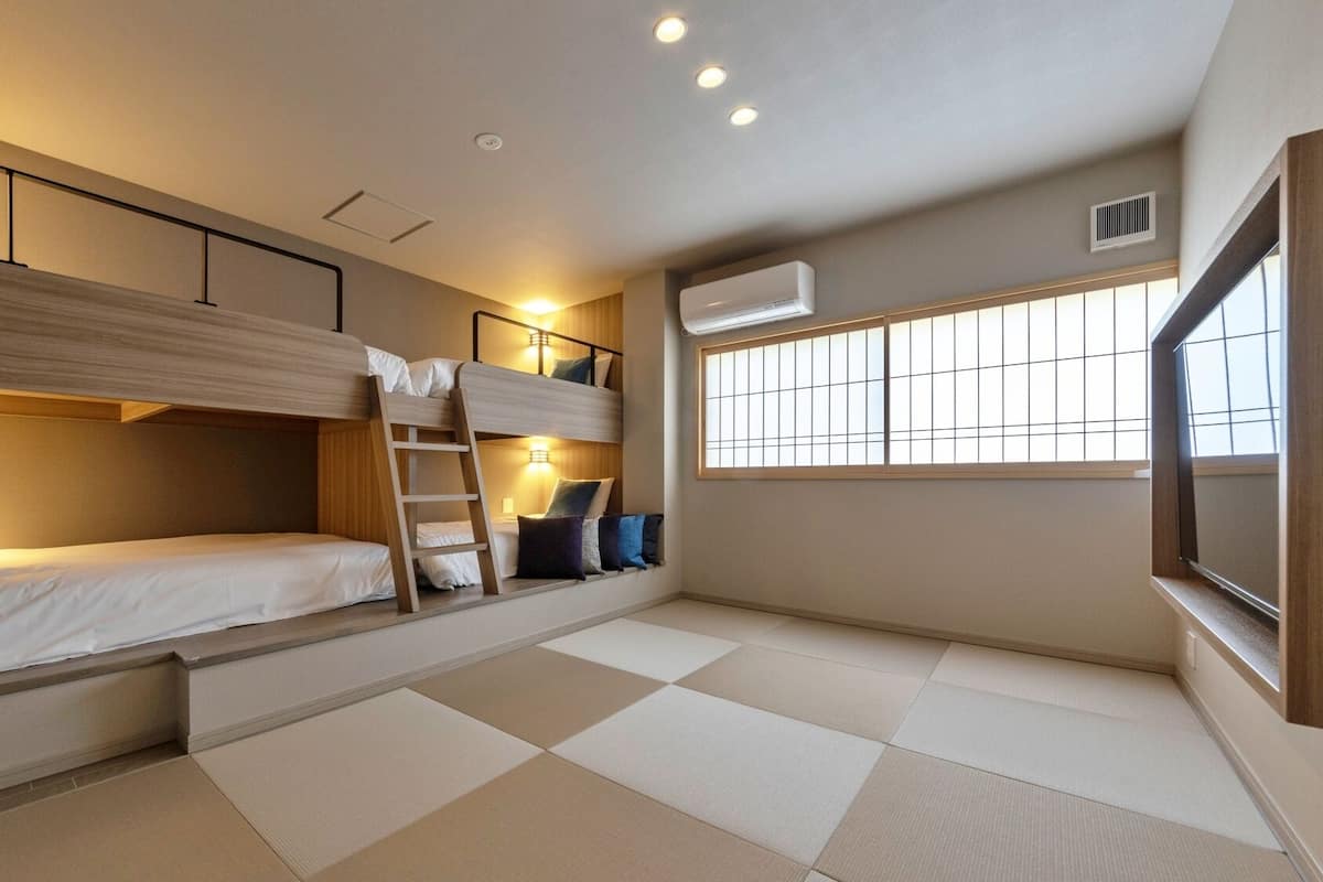 A bunk bed room with a ladder, a window with blinds, and an air conditioning unit.