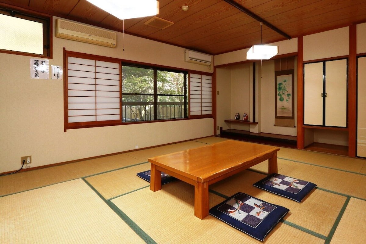 A traditional Japanese room with tatami flooring, a wooden table, sliding doors, and a view through a shoji screen.