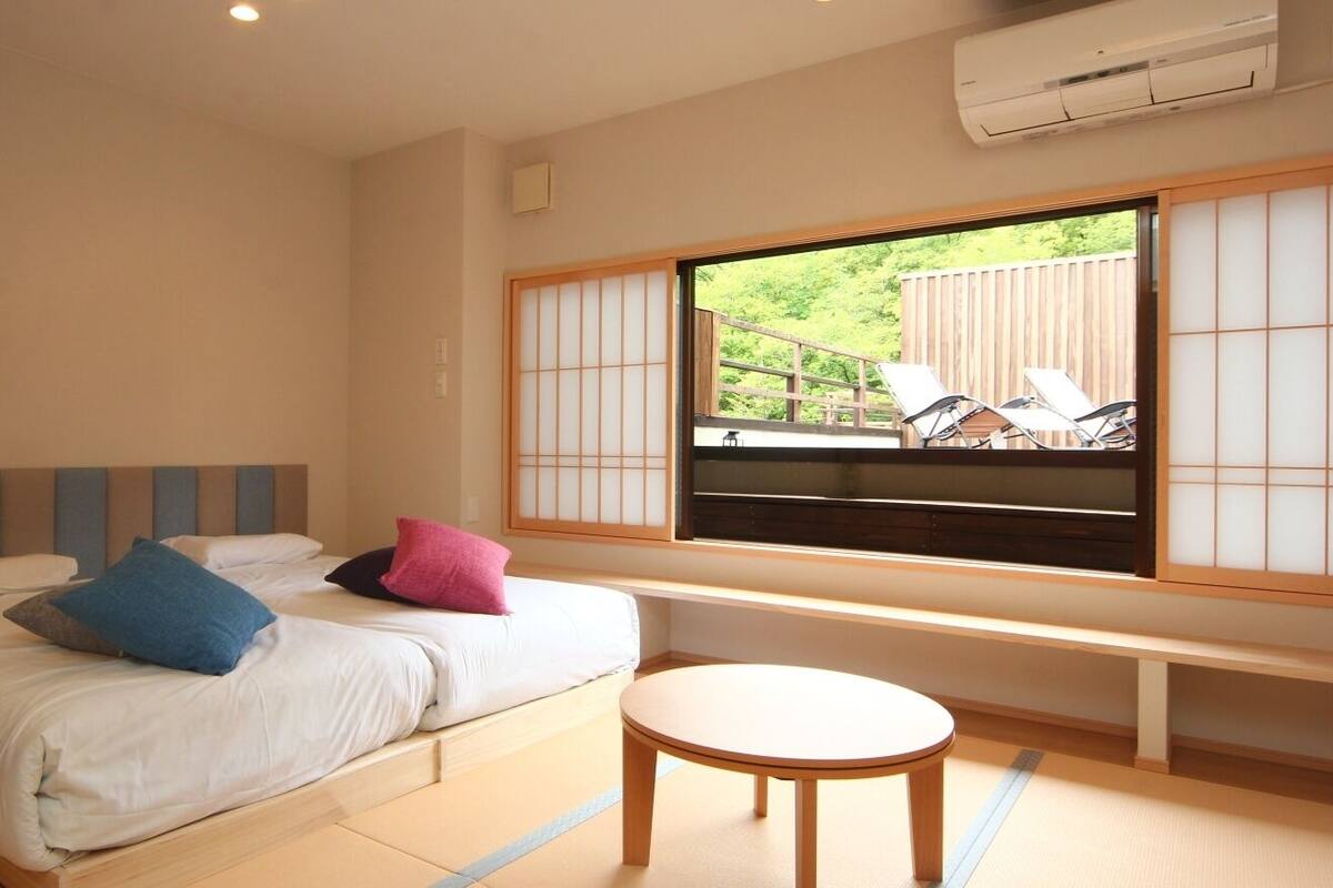 A bedroom with a bed, pillows, a round table, a window with a view of outdoor furniture, and a sliding door.