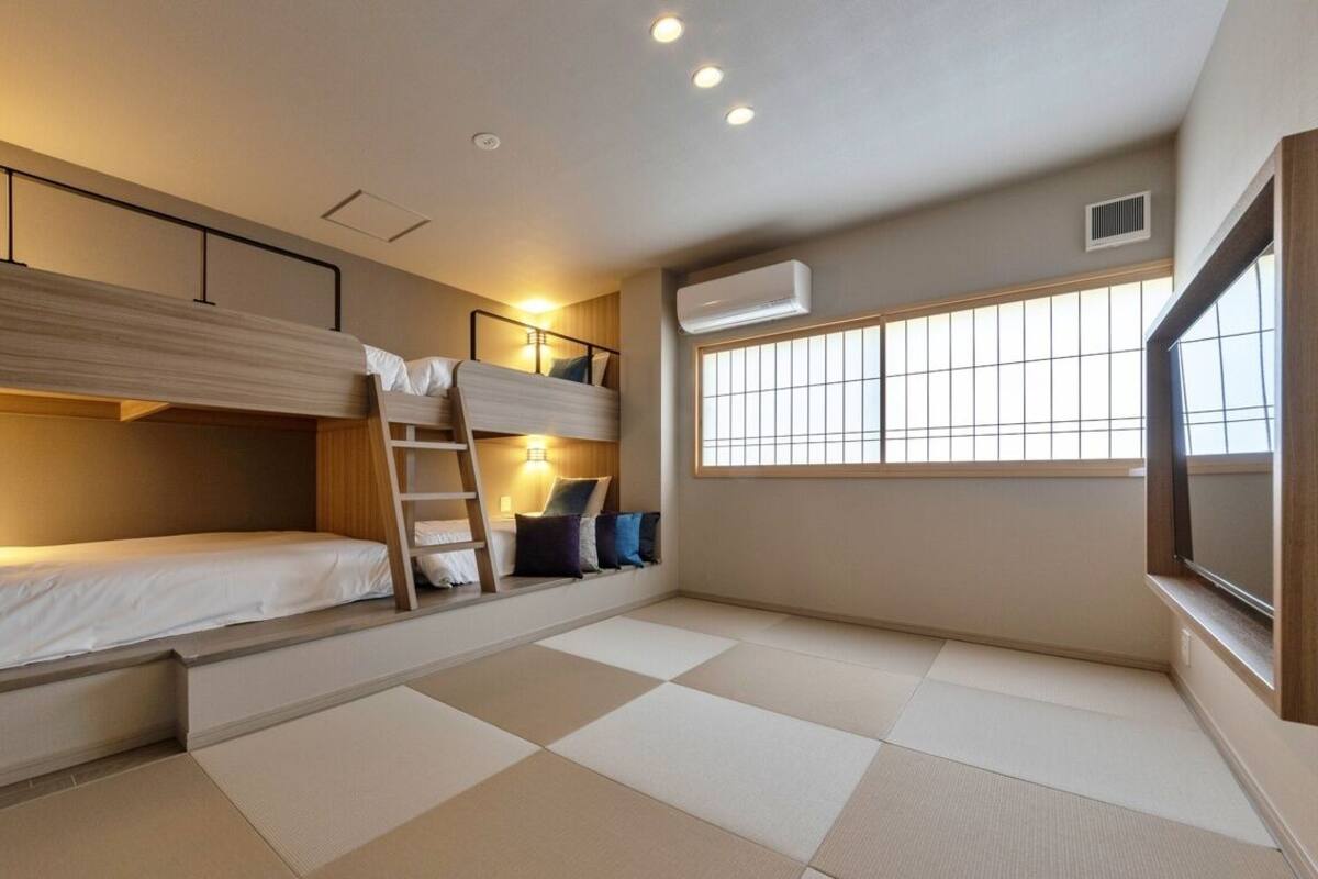 A room with bunk beds, a ladder, a window with blinds, and an air conditioning unit.