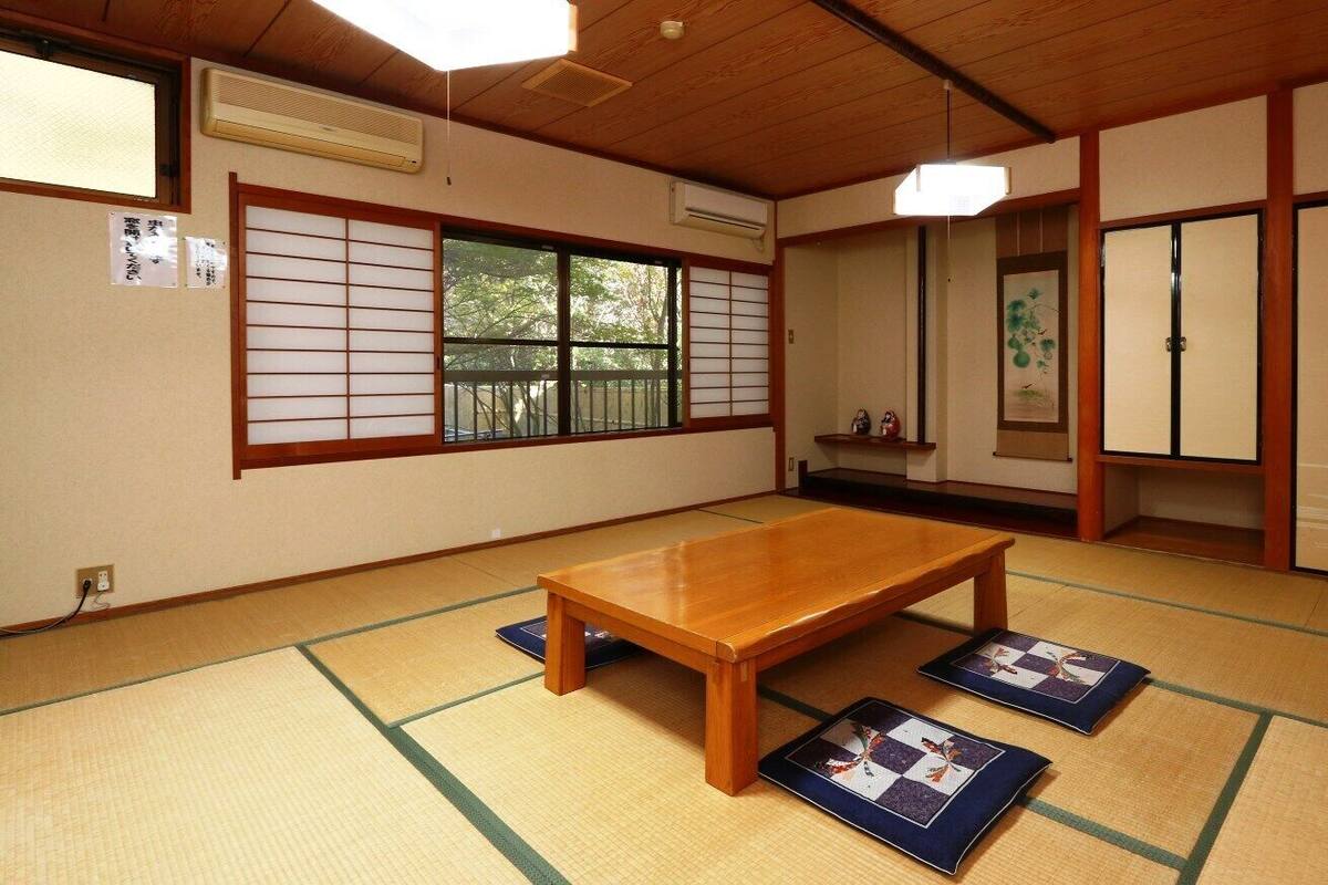 A traditional Japanese room with tatami flooring, a wooden table, sliding doors, and a view through a shoji screen.