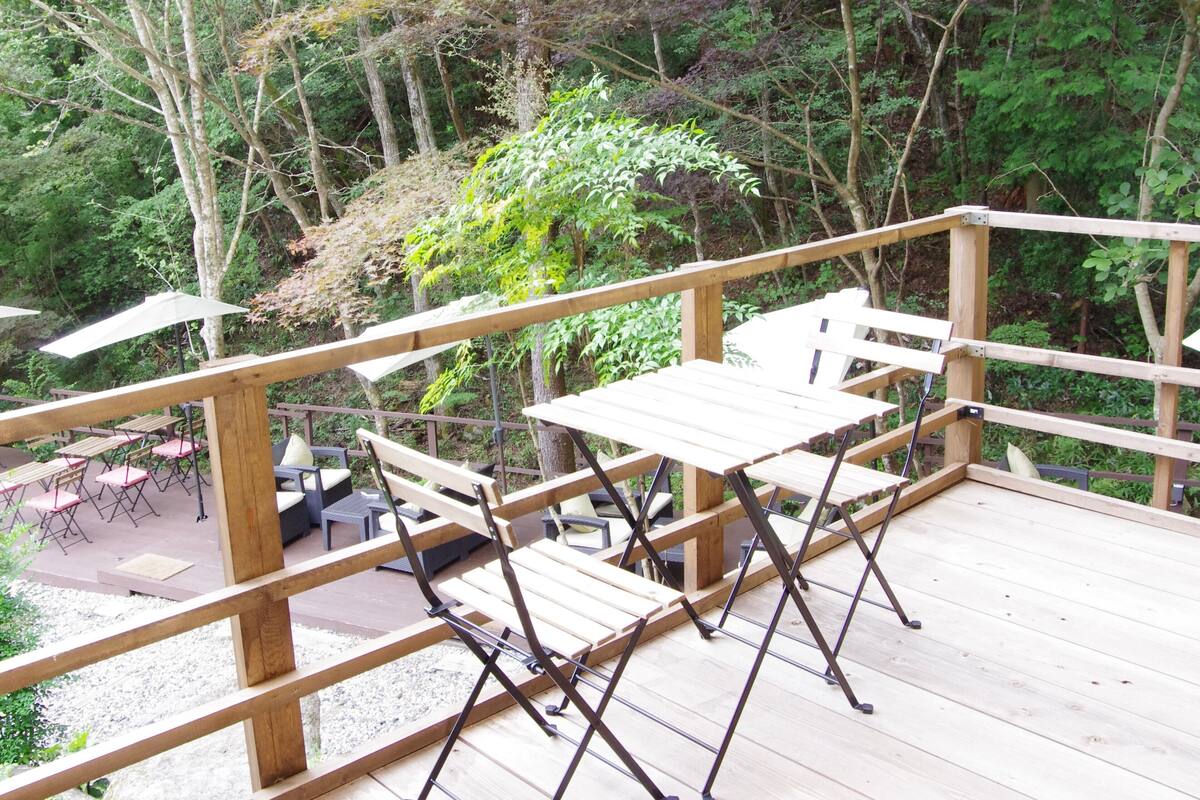 A wooden deck with tables and chairs, surrounded by dense forest.