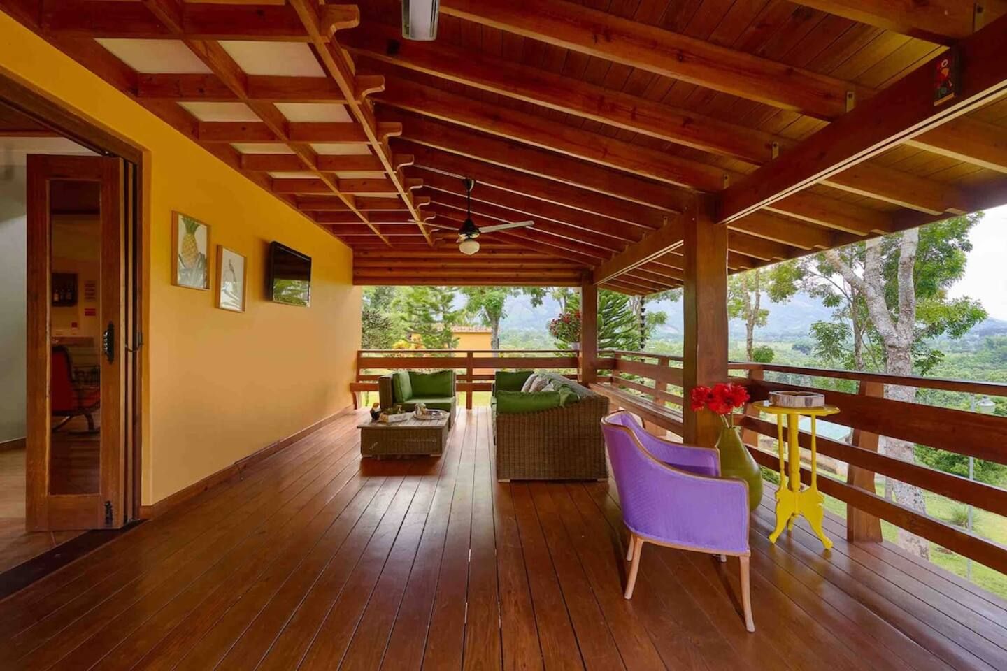 Une véranda couverte avec un plancher en bois, un canapé, un fauteuil et une petite table sur laquelle est posé un vase de fleurs.