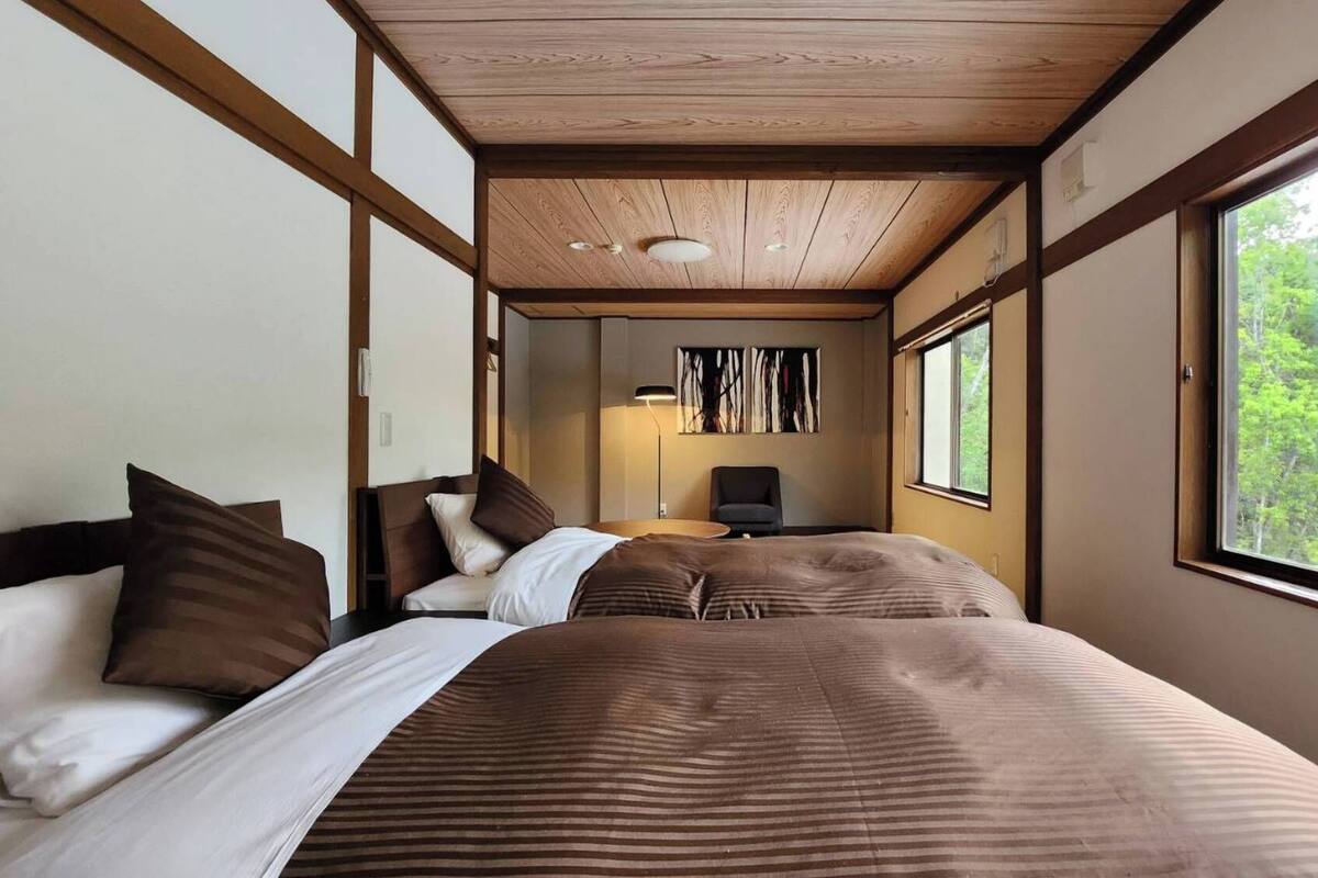 A room with two beds, a desk, and a window with a view of trees.