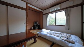A room with a bed, a wooden desk, a television, and a window with curtains.
