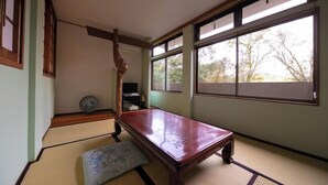 A tatami mat room with a wooden table, a futon bed, and large windows. - Nagahigawa (Miyazaki)