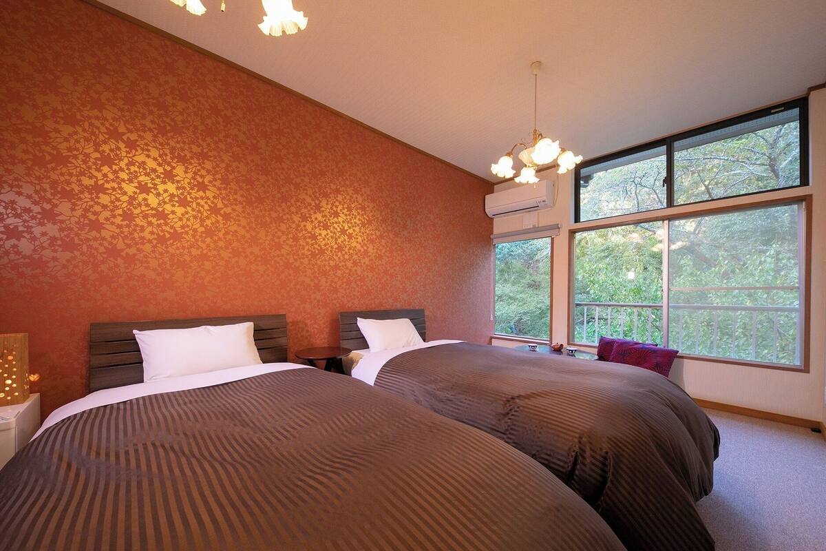 A bedroom with two beds, a large window, and a ceiling light fixture.