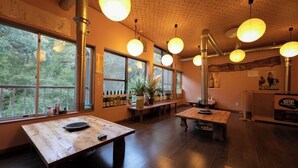 A restaurant interior with wooden tables, hanging spherical lights, and large windows offering a view of trees. - Nagahigawa (Miyazaki)