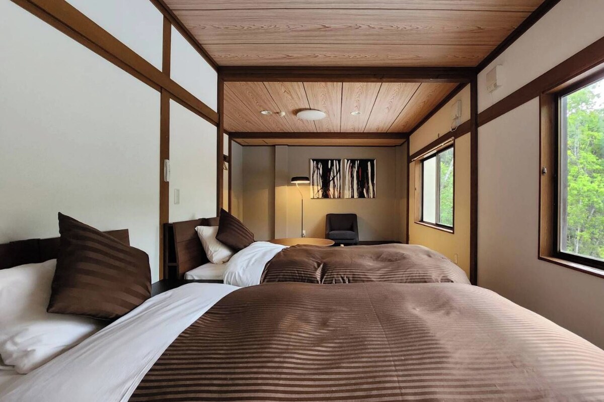 A room with two beds, a desk, and a window with a view of trees.