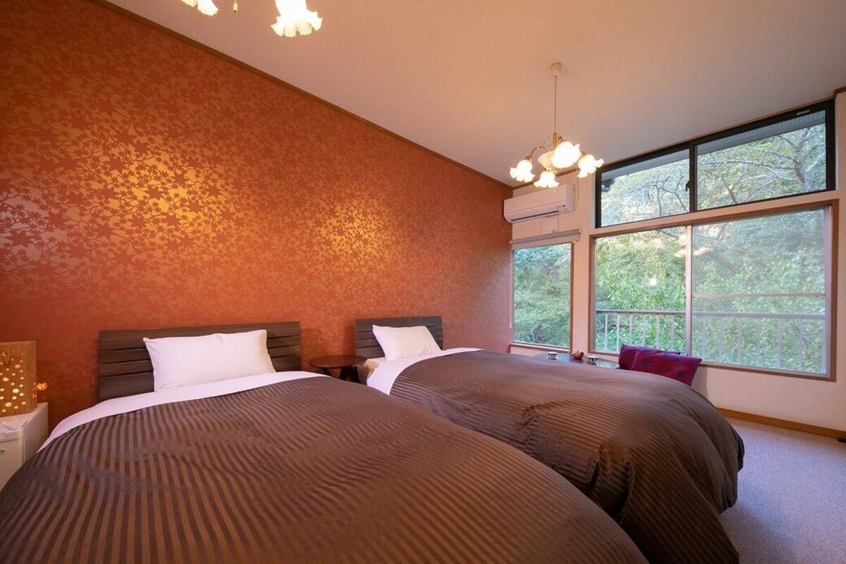 A bedroom with two beds, a large window, and an air conditioning unit.