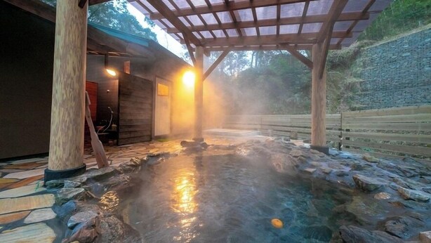 A hot spring area with a wooden deck, stone flooring, and a stone wall in the background. - Nagahigawa (Miyazaki)