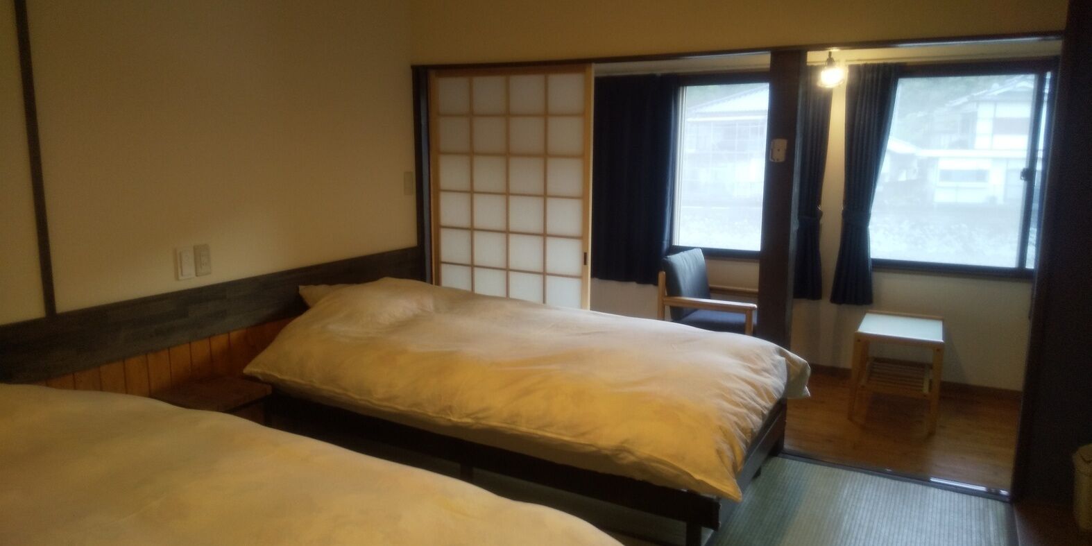 Una habitación con dos camas, un panel corredero shoji, una silla y una mesita.