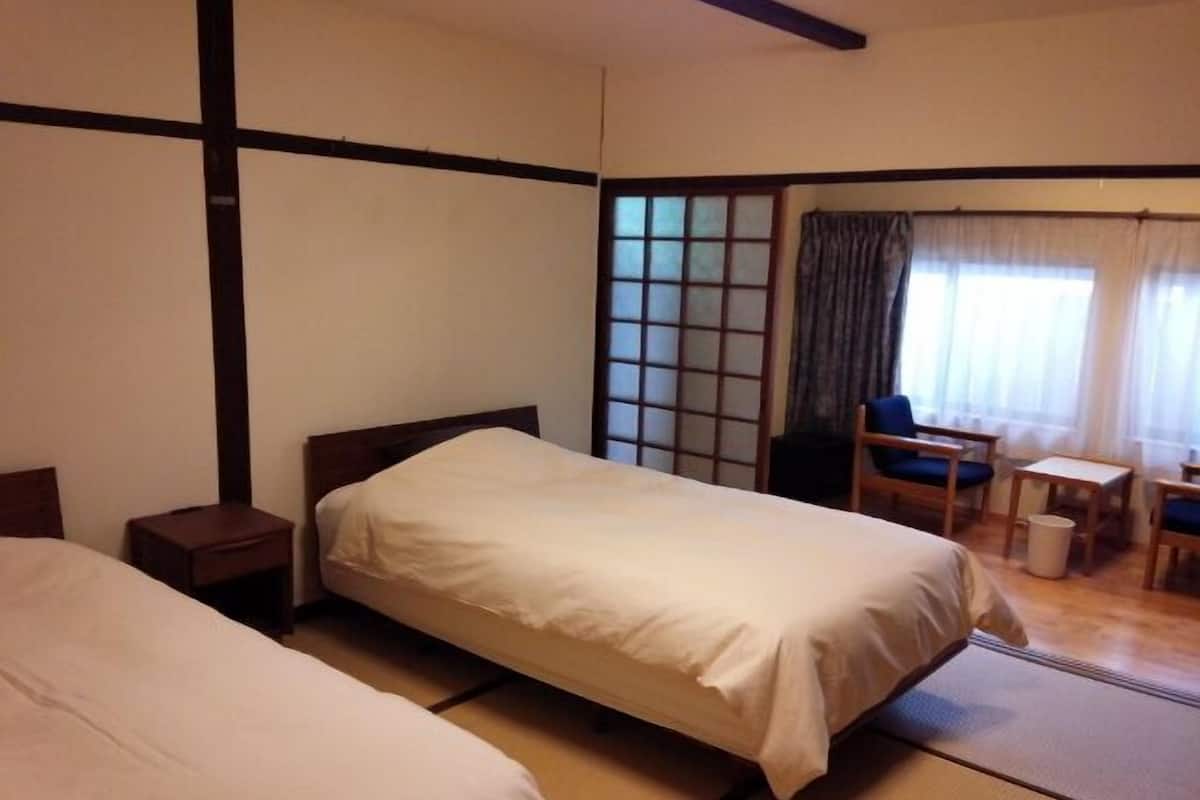 A traditional Japanese-style room with tatami flooring, a low wooden bed, a small table, and a chair.