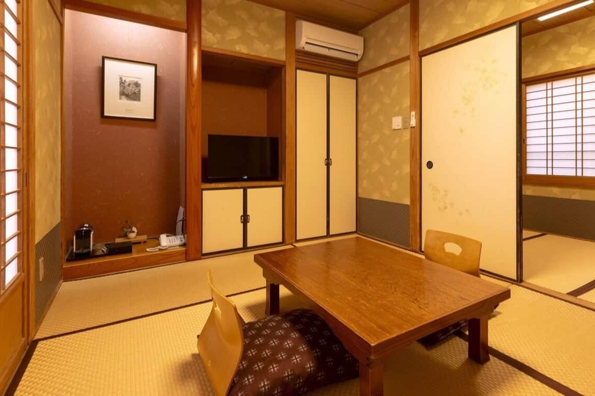 Ett traditionellt japanskt rum med tatamimattor på golvet, ett träbord, en tv och skjutdörrar.