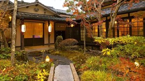 A traditional Japanese building with a garden, stone lanterns, and a wooden pathway.