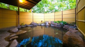 A traditional Japanese onsen with a stone bath surrounded by rocks and bamboo walls.