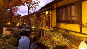 A traditional Japanese garden with a koi pond, stone lanterns, and a wooden building with shoji screens.