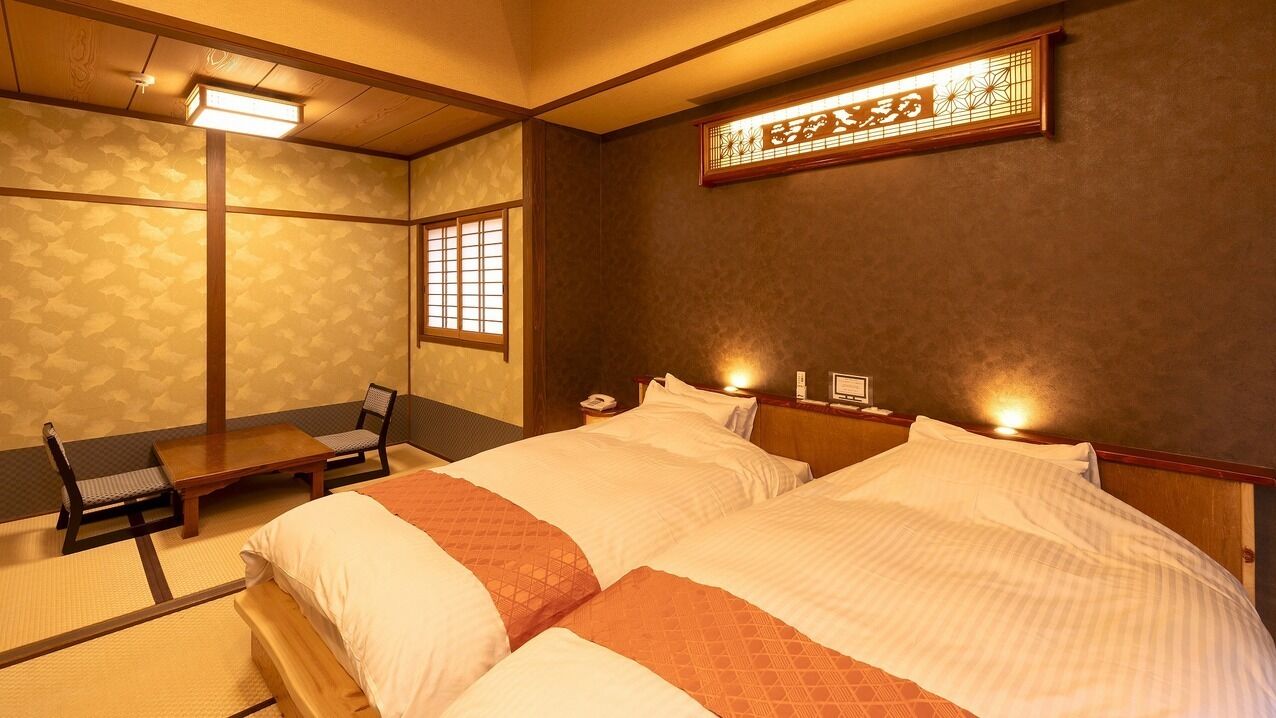 A traditional Japanese-style room with tatami flooring, a low wooden bed with white bedding, a small table, and a chair.