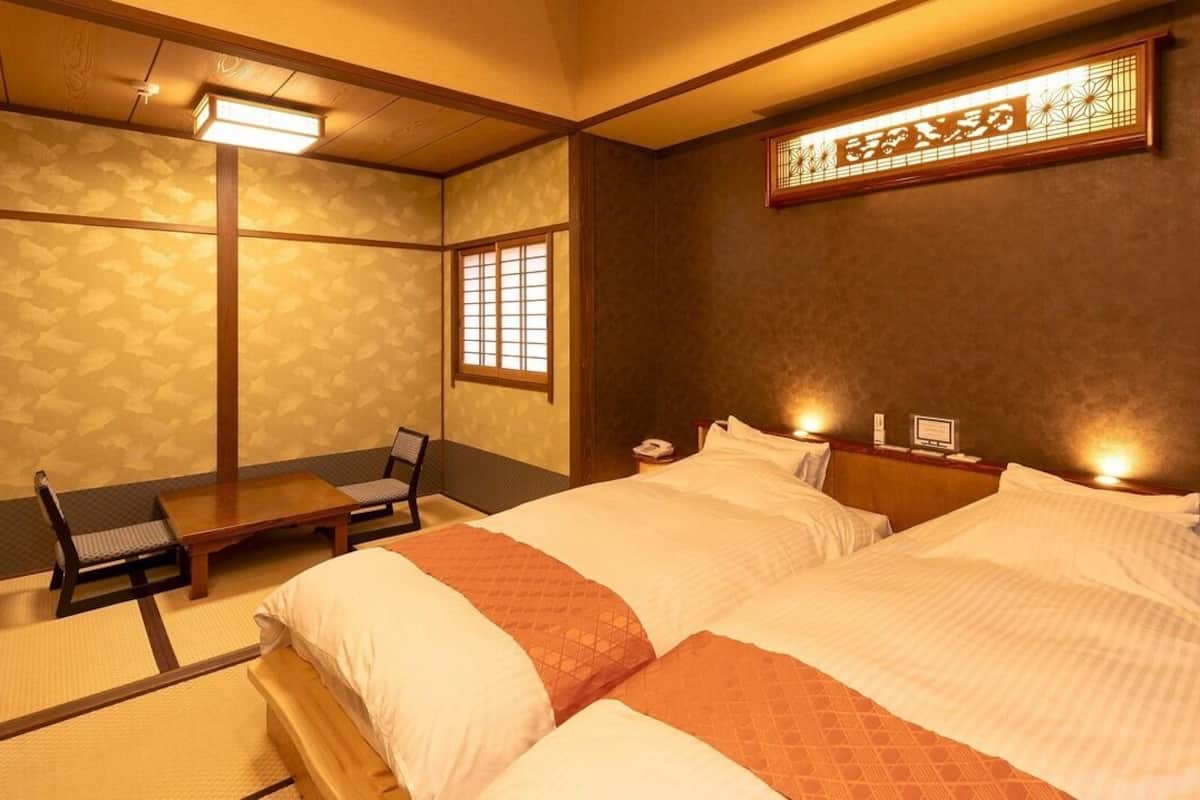 Ett traditionellt japanskt rum med tatamimattor på golvet, en låg säng av trä med vita sängkläder, ett litet bord och en stol.